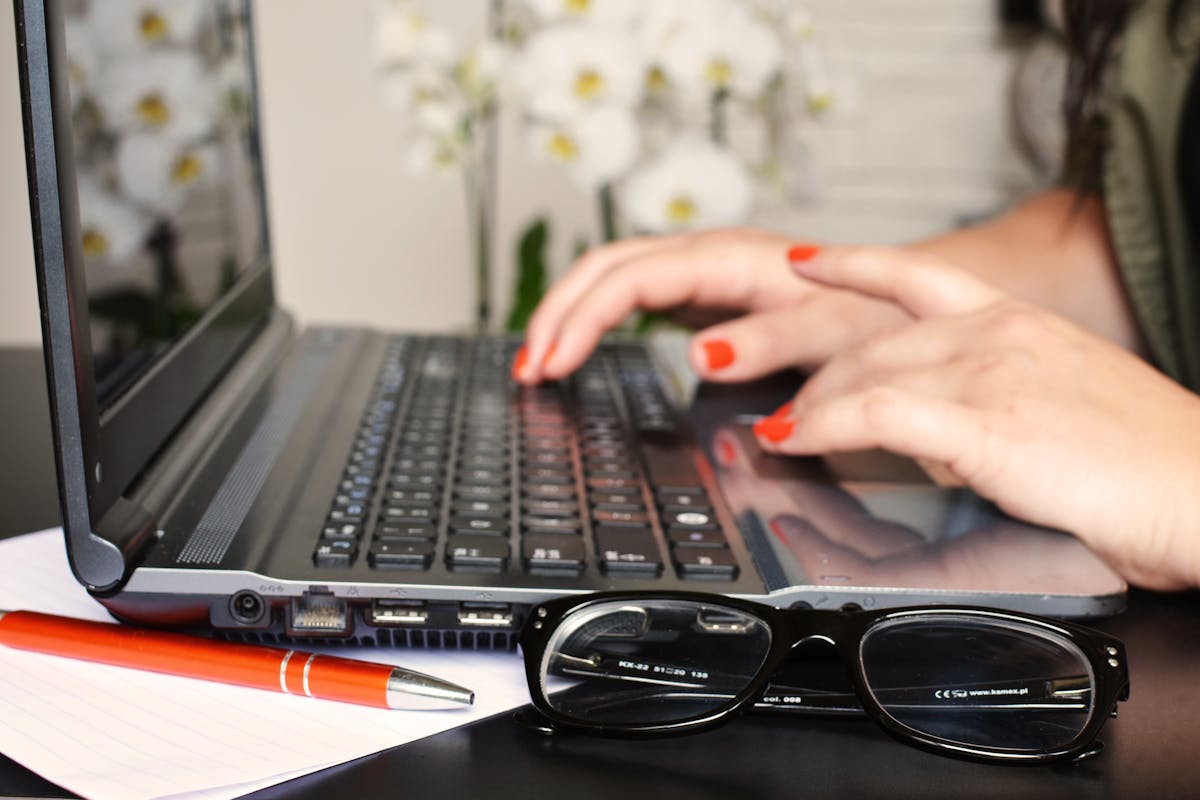 Woman editing text on a laptop with glasses and notepad