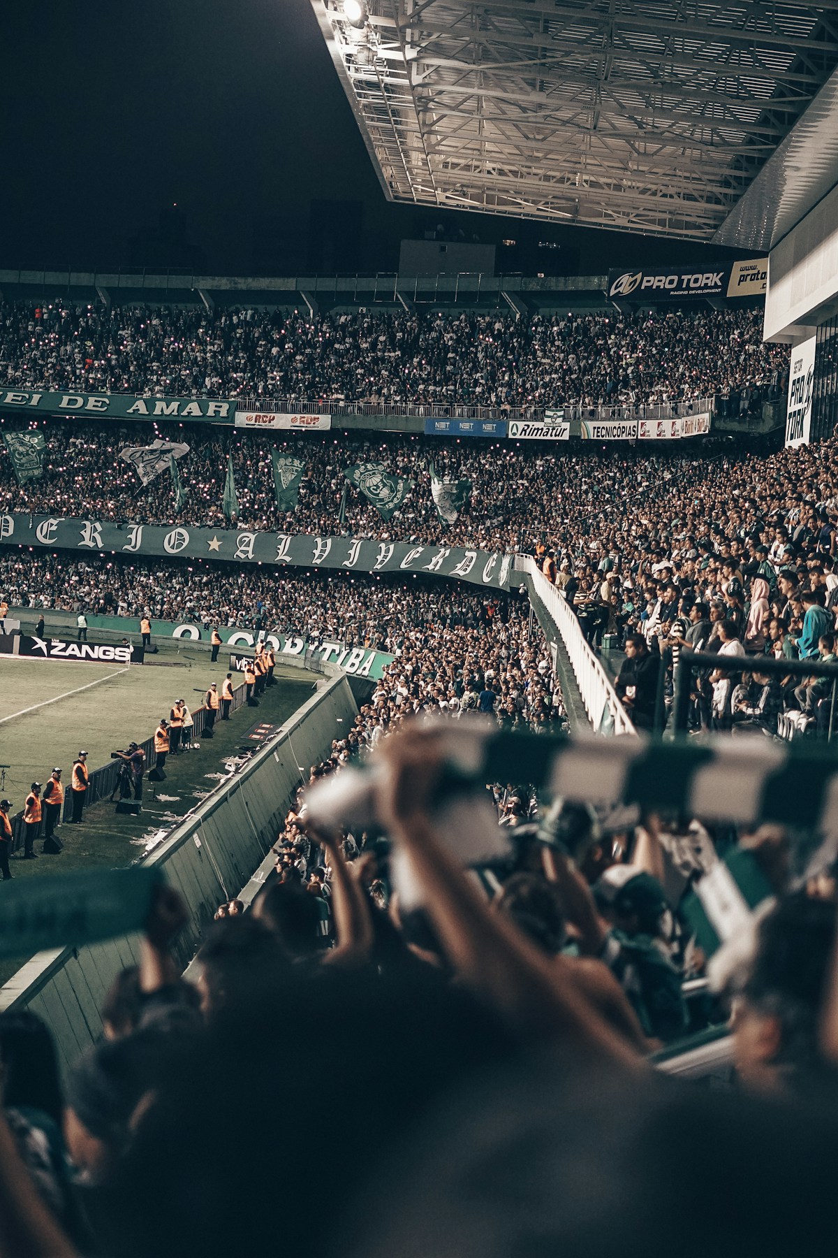 A packed football stadium at night, fans creating the atmosphere where nicknames are born