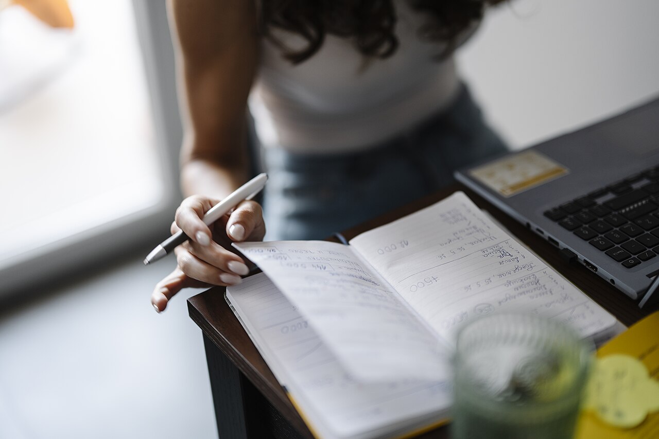 Person writing in a notebook at a desk — Photo by Shixart1985, CC BY 2.0, via Wikimedia Commons